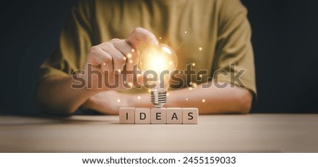 New idea concept with innovation and inspiration, hand touching on light bulb on wood block with Word Ideas, innovative technology in science and communication concept. Royalty-Free Stock Photo #2455159033