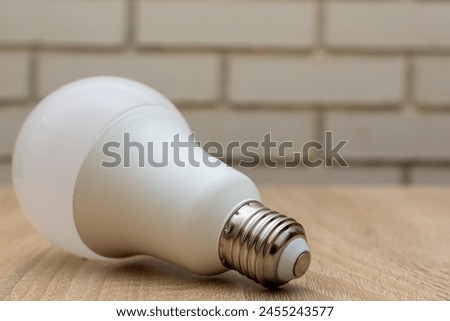 A beige light bulb, possibly a fluorescent lamp or compact fluorescent lamp, rests on a hardwood table, creating a beautiful still life photography composition