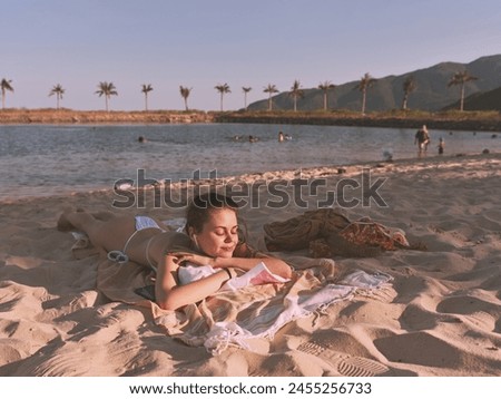 Woman in bikini relaxing on towel at beach next to body of water on sunny day vacaation landscape