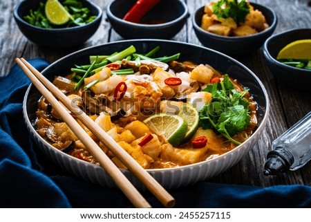Tom Yum - Thai soup with halibut nuggets and rice noodles on wooden table 