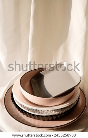Dishes and bowls are stacked on each other with a white fabric background. Dried kitchenware with sunlight in a home kitchen. Concept of food, cooking, clean plates, and shadow. Kitchenware top view.