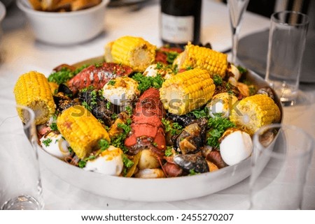 A slightly zoomed-in picture of a large platter of seafood boil with various shellfish on a set table, with glasses and plates visible in the background
