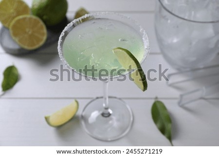 Delicious Margarita cocktail in glass and limes on white wooden table