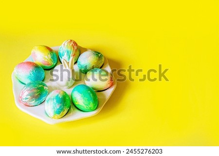 pastel colored Easter eggs delicate yellow, blue, pink, orange, green with blur beautiful decorated eggs lie on a porcelain plate with a white rabbit on a rich yellow background with space for text