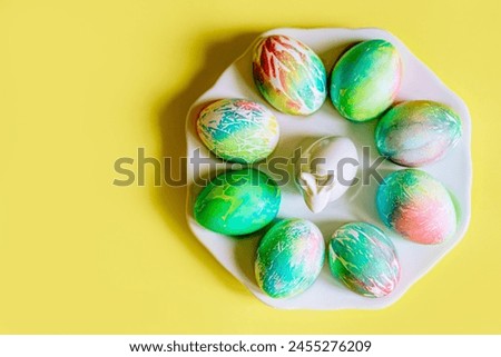 pastel colored Easter eggs delicate yellow, blue, pink, orange, green with blur beautiful decorated eggs lie on a porcelain plate with a white rabbit on a rich yellow background with space for text
