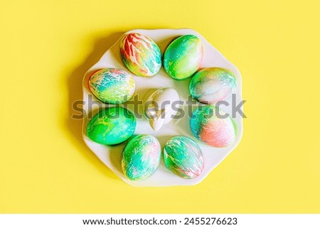 pastel colored Easter eggs delicate yellow, blue, pink, orange, green with blur beautiful decorated eggs lie on a porcelain plate with a white rabbit on a rich yellow background