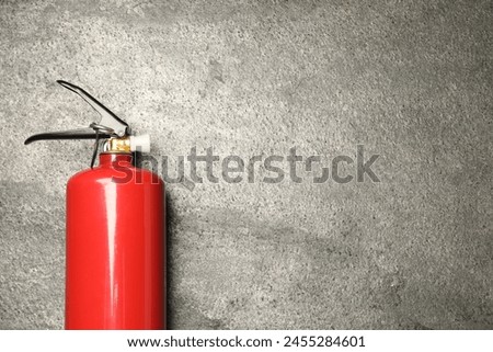 One red fire extinguisher on gray textured background, top view. Space for text