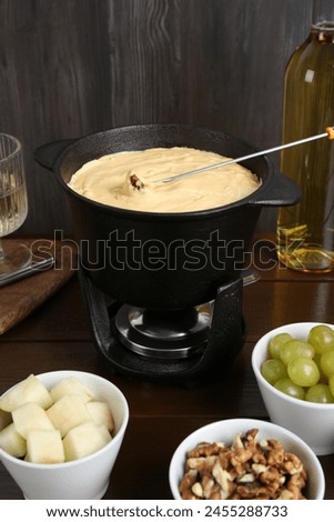 Fondue pot with tasty melted cheese, fork, wine and different snacks on wooden table