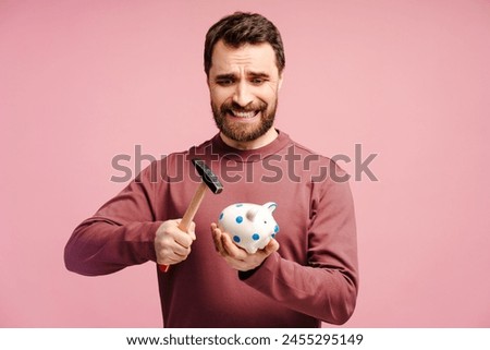 Scared bearded man holding iron and broking piggy bank, isolated over pink studio background. Money box, savings concept