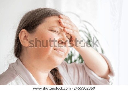 diseased mature woman experiences severe headache, holding head, Hot flashes during menopause, Decreased memory and concentration, feeling nervous, Feeling tired, exhausted, menopause, midlife crisis Royalty-Free Stock Photo #2455302369