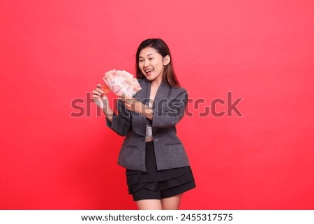 gesture of chinese office woman, candid smile, both hands holding credit cards and money, wearing a jacket and skirt on a red background. for financial, business and advertising concepts