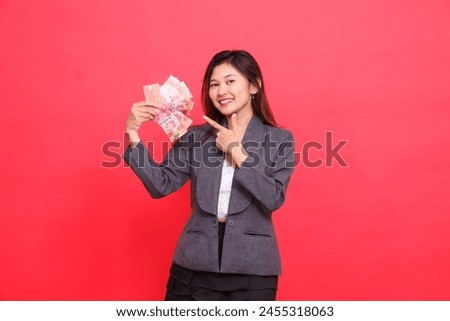 indonesia office woman smiling expression holding credit, debit card and money while pointing it at the camera wearing gray jacket and red skirt. for transaction, business and advertising concepts