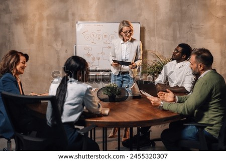 Senior businesswoman with tablet standing near whiteboard at conference room at corporate firm, presenting and pitching business ideas to multicultural investors. Manager having seminar at boardroom. Royalty-Free Stock Photo #2455320307