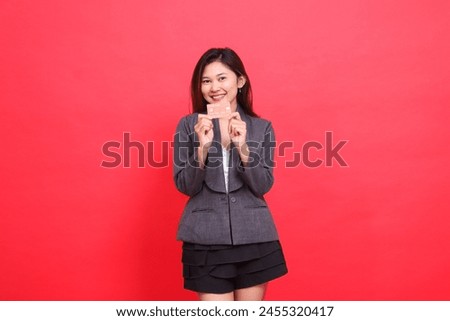 Cheerful Asian office woman's expression with both hands holding a debit credit card wearing a jacket and skirt on a red background. for financial, business and advertising concepts