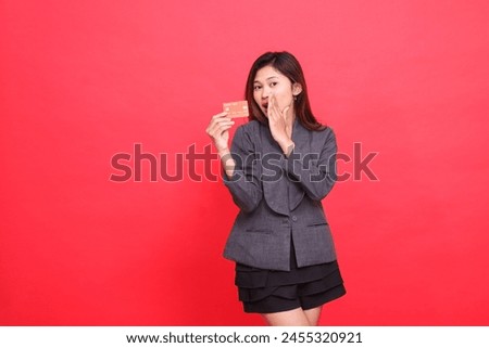 indonesia businesswoman expression stunned whispering hand to mouth and holding debit credit card wearing jacket and skirt on red background. for financial, business and advertising concepts
