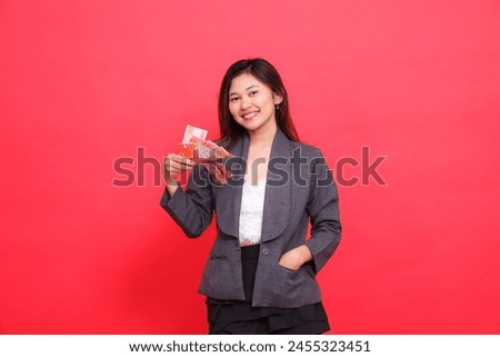 Cheerful Asian office woman expression holding debit credit card and money and putting money in pocket for camera wearing gray jacket and red skirt. for transaction, business and advertising concepts