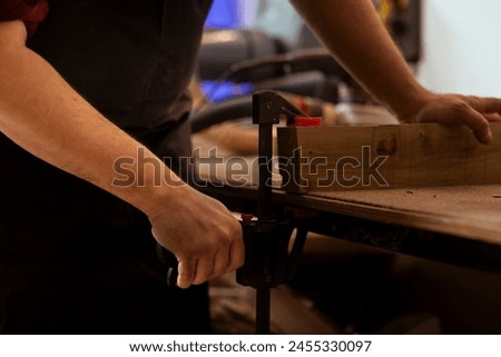 Woodworker using bench vise to hold lumber block, starting furniture assembling in workshop, close up shot. Craftsperson in joinery using vice tool to clamp piece of wood before carving it Royalty-Free Stock Photo #2455330097