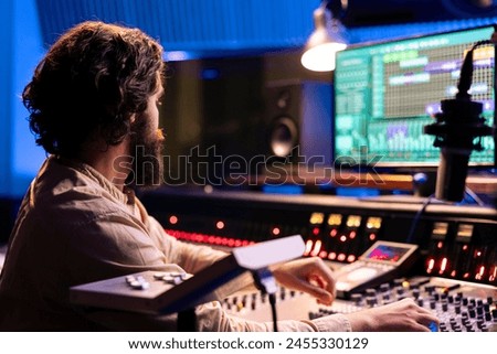 Sound designer editing music with digital audio software on pc, recording and processing sounds in control room. Young technician producing music with mixing console and faders.