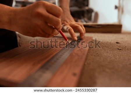 Craftsperson using ruler to take measurements of plank used to make wood furniture in carpentry shop. Woodworking expert drawing with pencil on wooden board to determine where to make cut, close up Royalty-Free Stock Photo #2455330287