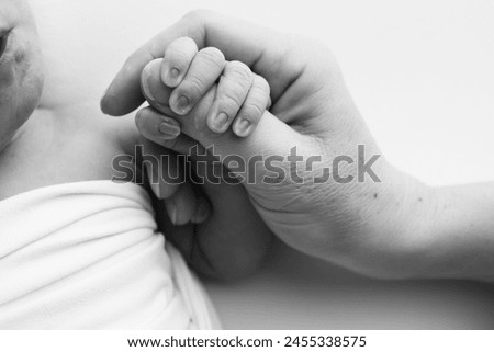Close-up little hand of child and palm of mother and father. The newborn baby has a firm grip on the parent's finger after birth. A newborn holds on to mom's, dad's finger. Black and white photo. 
