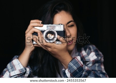 Close-up of a young woman taking photos with analog camera on a black background.
