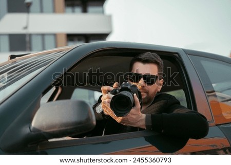 Private investigator sitting in the car and taking pictures, wearing black jacket and sunglasses 