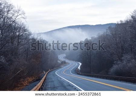 A winding road surrounded by trees and mountains in Pennsylvania. Picture taken on a winter morning, trees covered in ice with a foggy atmosphere