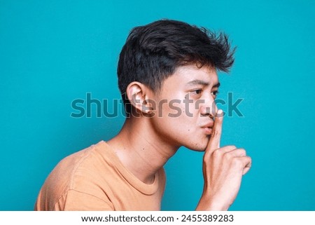Side view of young Asian man keeps finger on lips, asks not tell secret information or keep silence