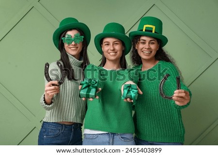 Beautiful young women in leprechaun hats with gift boxes and horseshoes on green background. St. Patrick's Day celebration