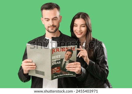 Cool young couple reading magazine on green background