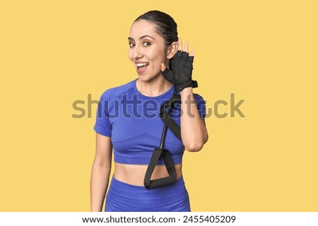 Athletic young Caucasian woman with resistance band on studio background trying to listening a gossip. Royalty-Free Stock Photo #2455405209