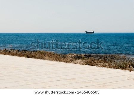 A grounded ship in the Mediterranean Sea, with a promenade along the blue sea and a rocky coastline in Paphos, Cyprus, under the bright sunny weather. Royalty-Free Stock Photo #2455406503