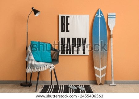 Surfboard, picture, armchair and paddle near orange wall in room