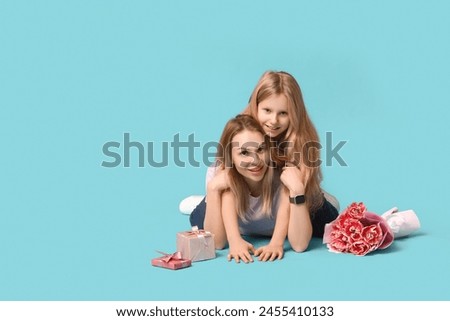 Cute little girl with her mom, gift boxes and bouquet for Mother's Day lying on blue background