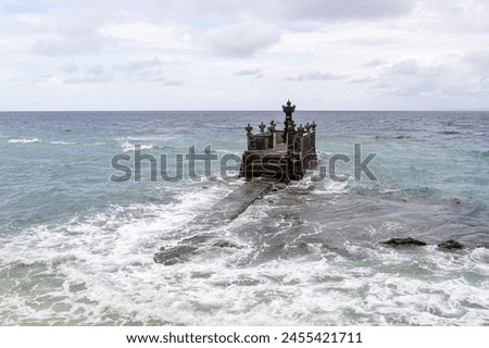 A Balinese sea temple stands on a rocky outcrop as waves crash around it under a cloudy sky Royalty-Free Stock Photo #2455421711