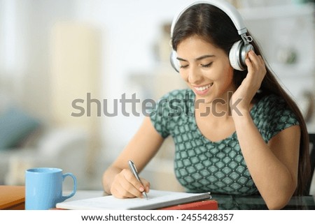 Happy student listening lesson with headphone and taking notes at home