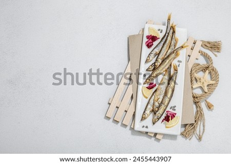 Smoked smelt with fresh lemon and herbs. Salted fish with marine decor. Trendy pallet, sea rope. Hard light, dark shadow, light stone concrete background, top view Royalty-Free Stock Photo #2455443907