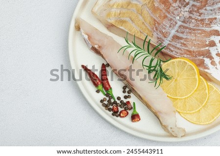 Raw pollock (Pollachius virens) fillet. Fresh fish for healthy food lifestyle. Lemon, rosemary, sea salt, chili, black peppercorn. Light stone concrete background, flat lay, top view
