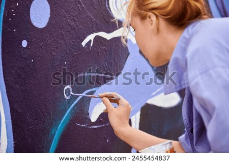 Female painter draws picture with paintbrush on canvas for outdoor street exhibition, close up back side view of female artist apply brushstrokes to canvas infusing life into outdoor art space