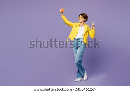 Full body young woman wear yellow shirt white t-shirt casual clothes glasses doing selfie shot on mobile cell phone post photo on social network isolated on plain purple background. Lifestyle concept
