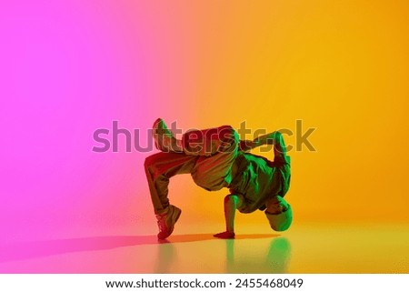 Young athlete man, dressed street style outfit dancing in motion in neon light against gradient pink-yellow background. Concept of art, hobby, sport, creativity, fashion and style, action. Ad