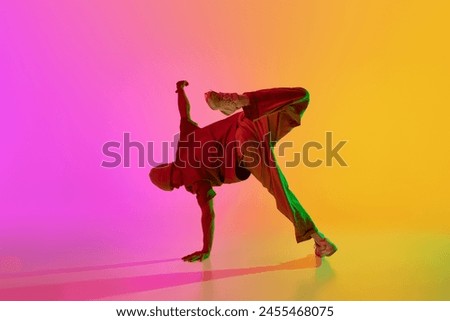 Dynamic photo of young, stylish dressed man breakdancer posing in neon light against gradient pink-yellow background. Concept of hobby, sport, creativity, fashion and style, motion, action. Ad