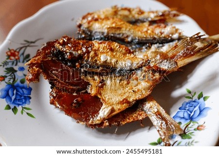 Fried spiced salted fish in a white plate on the table, food, stock photo.