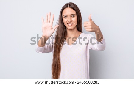 hispanic pretty woman smiling and looking friendly, showing number six or sixth with hand forward, counting down Royalty-Free Stock Photo #2455503285
