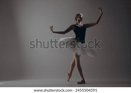Young ballerina in elegance white tutu and pointe shoes dancing against dark background. Graceful litted ballerina performing in dark. Ballet art, grace, flexibility, motion.