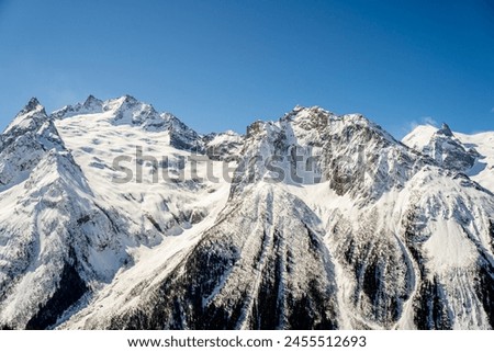 scenic natural picture with snow-capped huge mountain peaks and mountains, autumn bare trees, sky blue sky, snow lies on the mountain tops