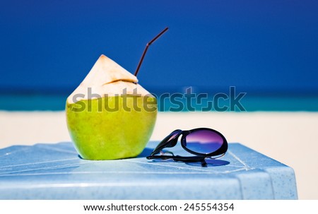 picture of fresh coconut cocktail and blue sunglasses on tropical beach 