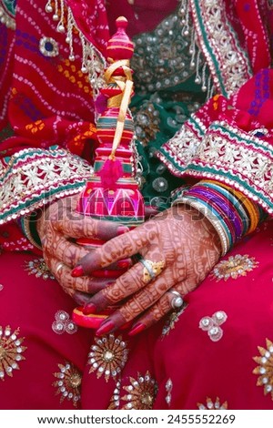 A close-up image showing the henna-decorated hands of an Indian bride, dressed in a vibrant pink sari and adorned with colorful glass bangles.