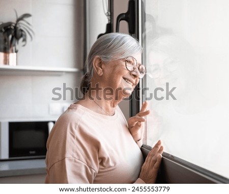 Happy middle aged senior retired woman standing near window, looking in distance, recollecting good memories enjoying peaceful moment Royalty-Free Stock Photo #2455553779
