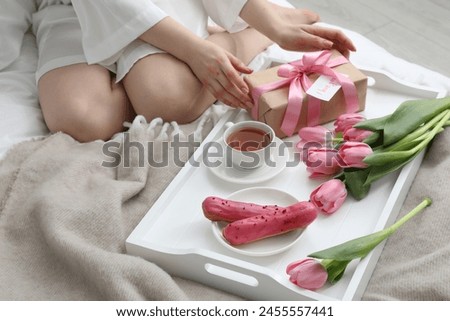 Tasty breakfast served in bed. Woman with gift box, tea, eclairs, flowers and I Love You card at home, closeup